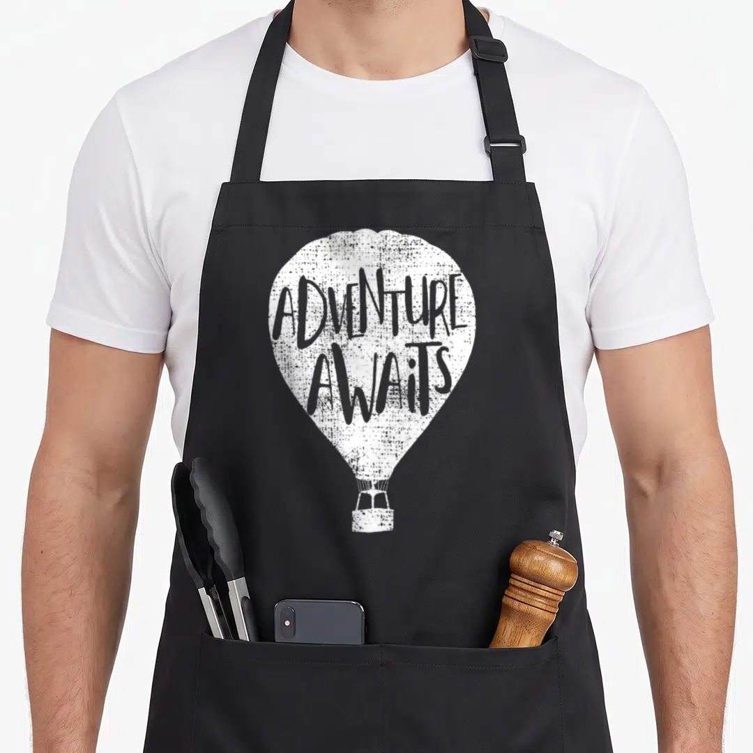 Aviator balloon apron - Distressed white hot air balloon with ADVENTURE AWAITS text on envelope — shown on a black cotton canvas apron against a white background