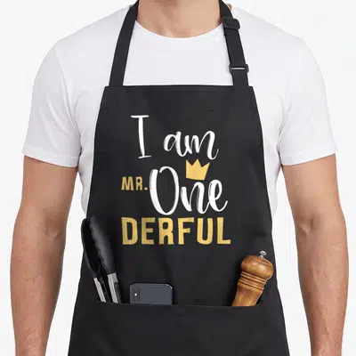 Onederful 1st birthday apron - I am MR. One DERFUL text with yellow crown in white and yellow typography — shown on a black cotton canvas apron against a white background