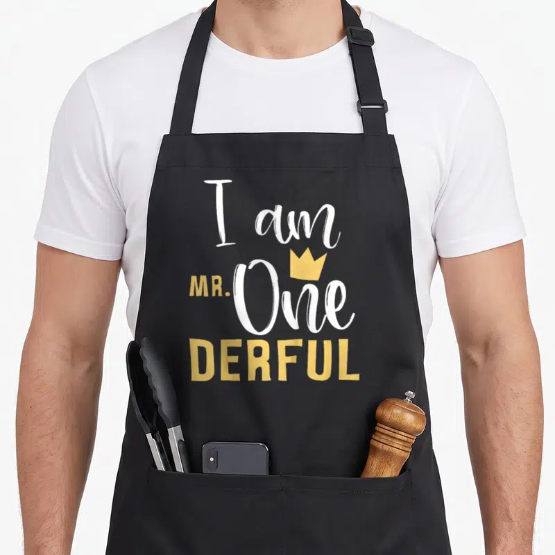 Onederful 1st birthday apron - I am MR. One DERFUL text with yellow crown in white and yellow typography — shown on a black cotton canvas apron against a white background