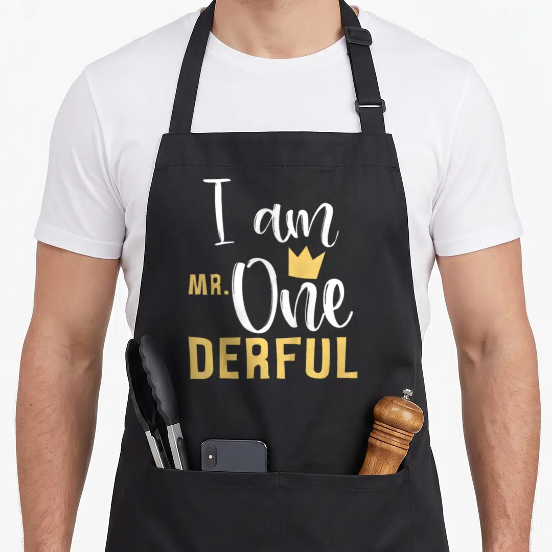 Onederful 1st birthday apron - I am MR. One DERFUL text with yellow crown in white and yellow typography — shown on a black cotton canvas apron against a white background