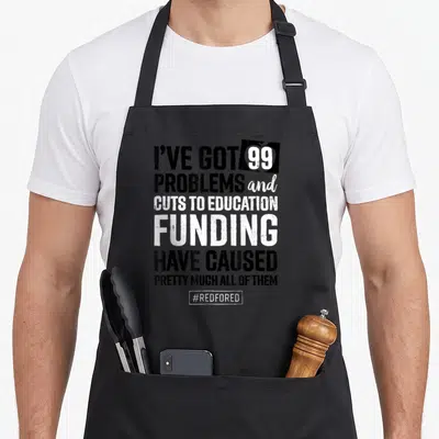 Colorado protest teacher apron - Stacked black and white text reading I've Got 99 Problems cuts to education funding — shown on a black cotton canvas apron against a white background
