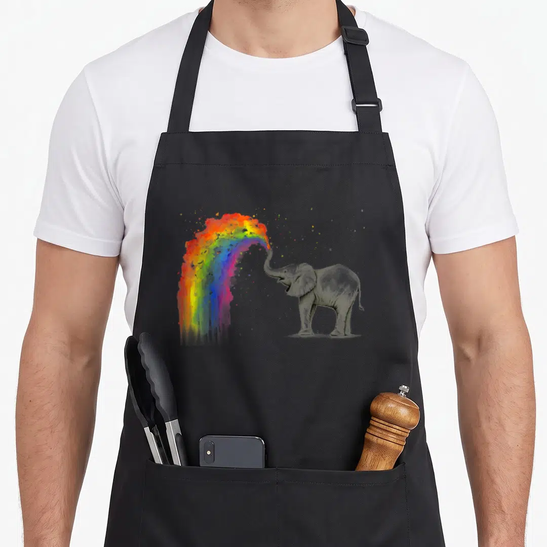 Spraying elephant print apron - Grey elephant spraying multicolored watercolor rainbow with red yellow blue and green — shown on a black cotton canvas apron against a white background