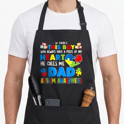 Awareness special aprons - So There's This Boy Dad Autism Awareness text with puzzle piece heart and colorful blocks — shown on a black cotton canvas apron against a white background