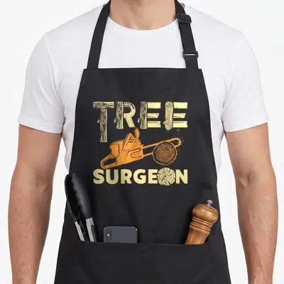 Tree arborist surgeon apron - Orange chainsaw cutting wood slice between tan log-style words TREE SURGEON — shown on a black cotton canvas apron against a white background