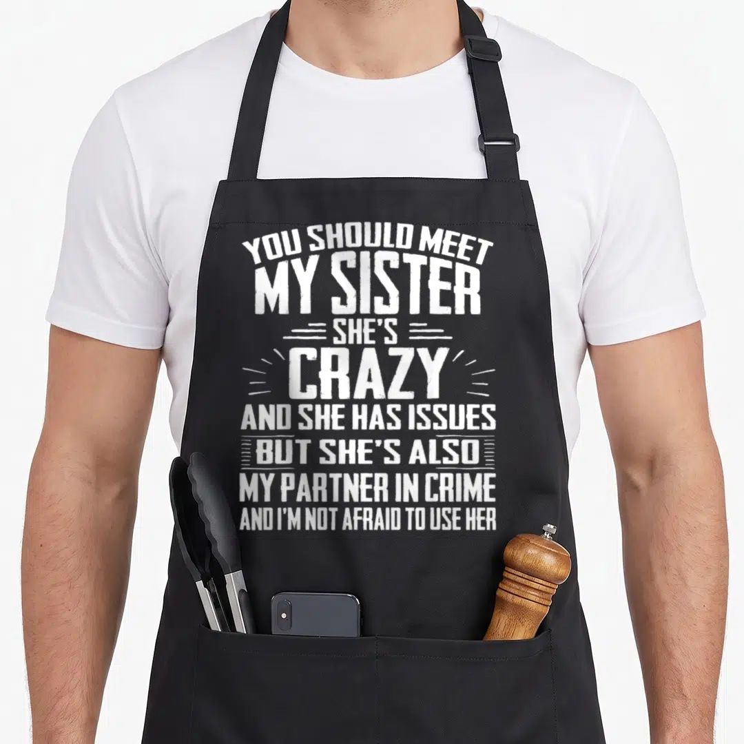 Sister nun apron - White stacked typography reading You Should Meet My Sister She's Crazy Partner In Crime — shown on a black cotton canvas apron against a white background