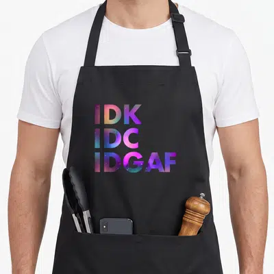 Cute idk idgaf apron - Stacked IDK IDC IDGAF text filled with purple blue pink and teal galaxy stars — shown on a black cotton canvas apron against a white background