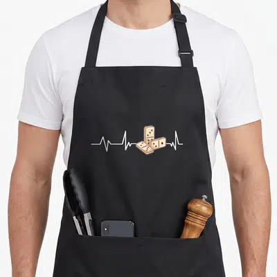 Heartbeat dominoes apron - Three beige domino tiles overlapping a white horizontal heartbeat line in cartoon style — shown on a black cotton canvas apron against a white background