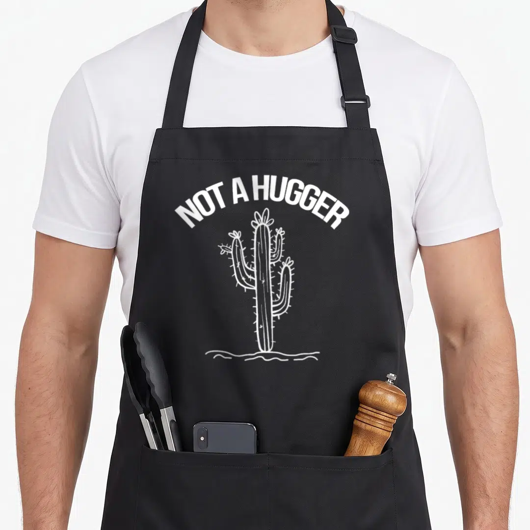 Hugger cactus apron - White line art cactus with arched text NOT A HUGGER above it — shown on a black cotton canvas apron against a white background