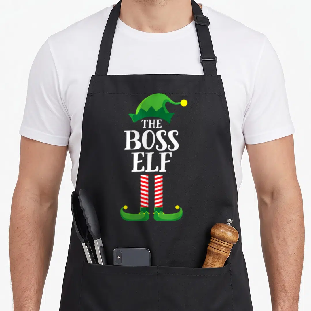 Elf boss apron - THE BOSS ELF text between green hat and red white striped legs with curled shoes — shown on a black cotton canvas apron against a white background