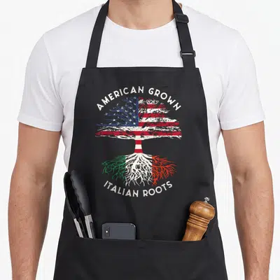 Grown american flag apron - Tree with US flag canopy and Italian flag roots bearing American Grown Italian Roots text — shown on a black cotton canvas apron against a white background