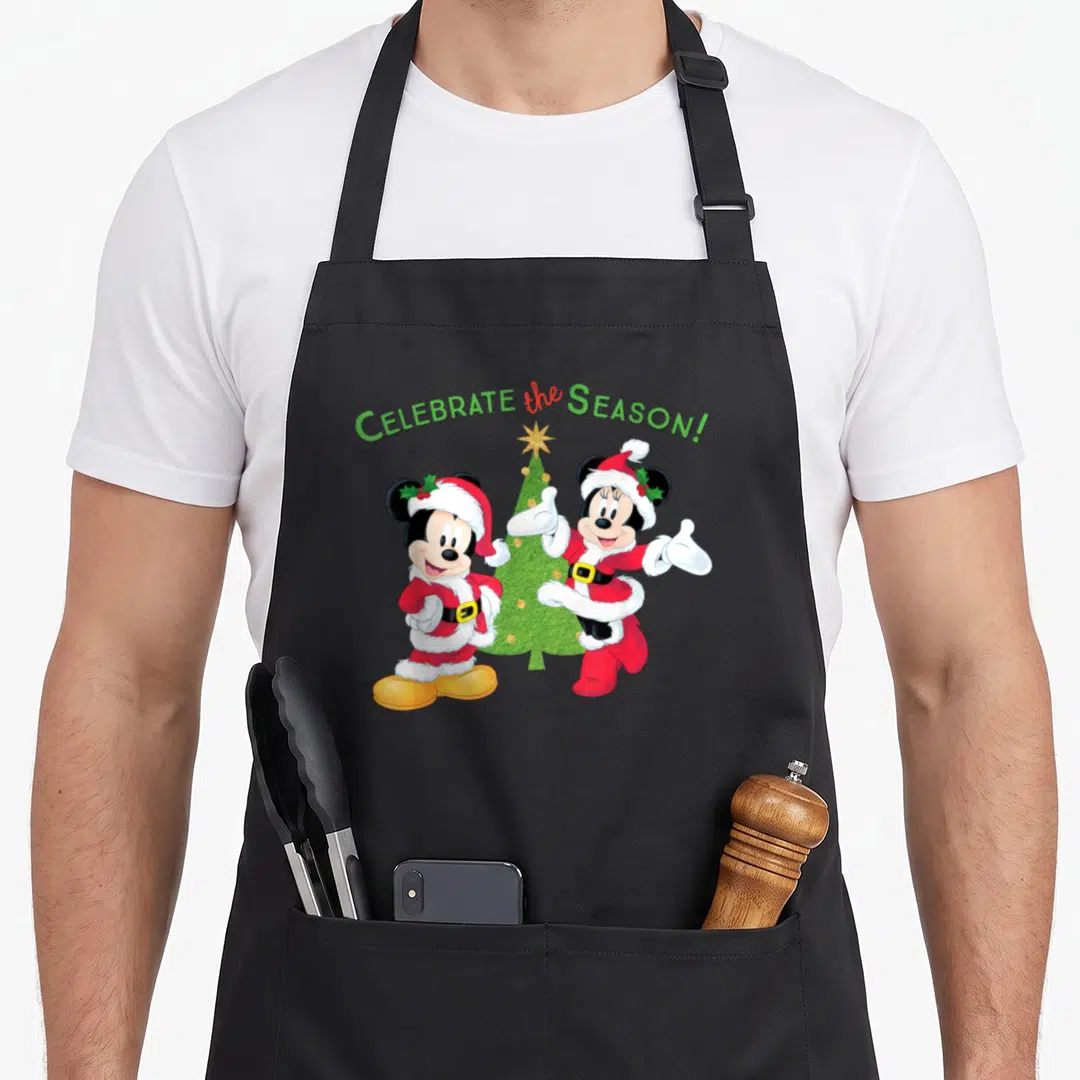 Santa holiday apron - Mickey and Minnie in Santa suits flanking a Christmas tree under arched text — shown on a black cotton canvas apron against a white background