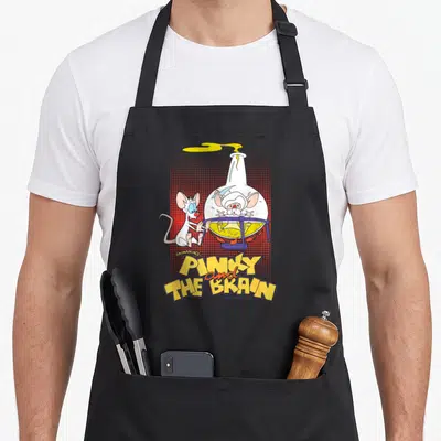 Pinky flask apron - Pinky and the Brain in yellow flask with red dotted background and bold title text — shown on a black cotton canvas apron against a white background