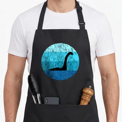 Nessie scotland apron - Black dinosaur silhouette inside a blue circle with horizontal stripes and distressed texture — shown on a black cotton canvas apron against a white background