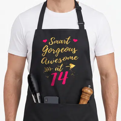 Gorgeous smart apron - Gold script text Smart Gorgeous Awesome at 14 with pink hearts and arrow graphics — shown on a black cotton canvas apron against a white background