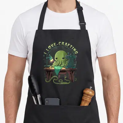 Cthulhu crafting apron - Green octopus sewing at desk with I LOVE-CRAFTING text arching above — shown on a black cotton canvas apron against a white background