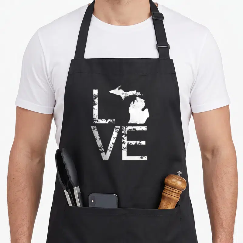 Map pride apron - Distressed white LOVE text with Michigan map replacing the letter O — shown on a black cotton canvas apron against a white background