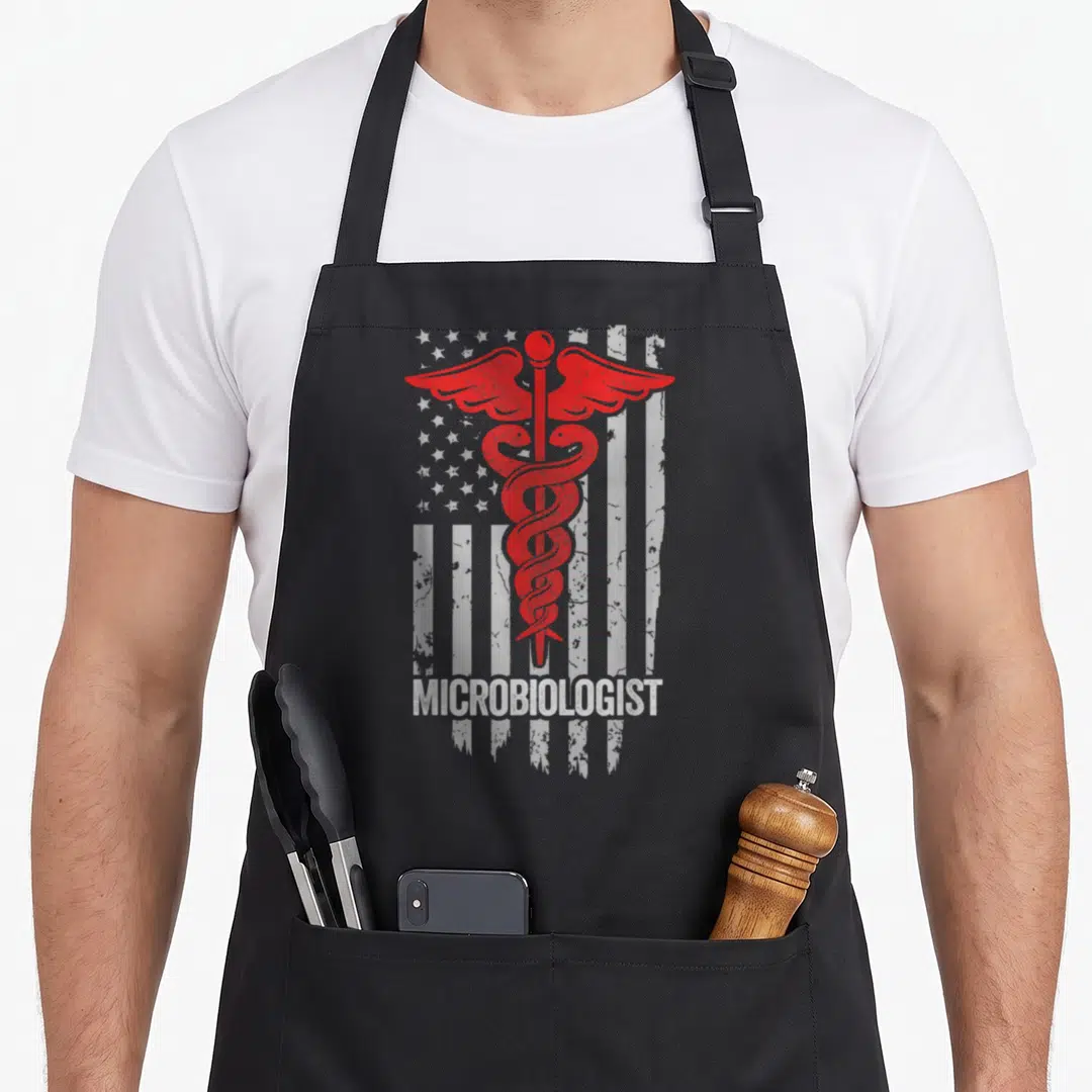 Microbiologist american flag apron - Red caduceus over distressed white flag with white MICROBIOLOGIST text at bottom — shown on a black cotton canvas apron against a white background