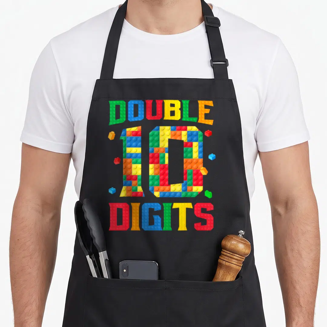 Builder master apron - Colorful brick text reading DOUBLE 10 DIGITS with scattered blocks in red blue yellow green — shown on a black cotton canvas apron against a white background