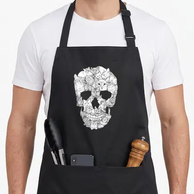 Cat skull skeleton apron - Skull shape formed by cluster of small cats in line art white grey black — shown on a black cotton canvas apron against a white background
