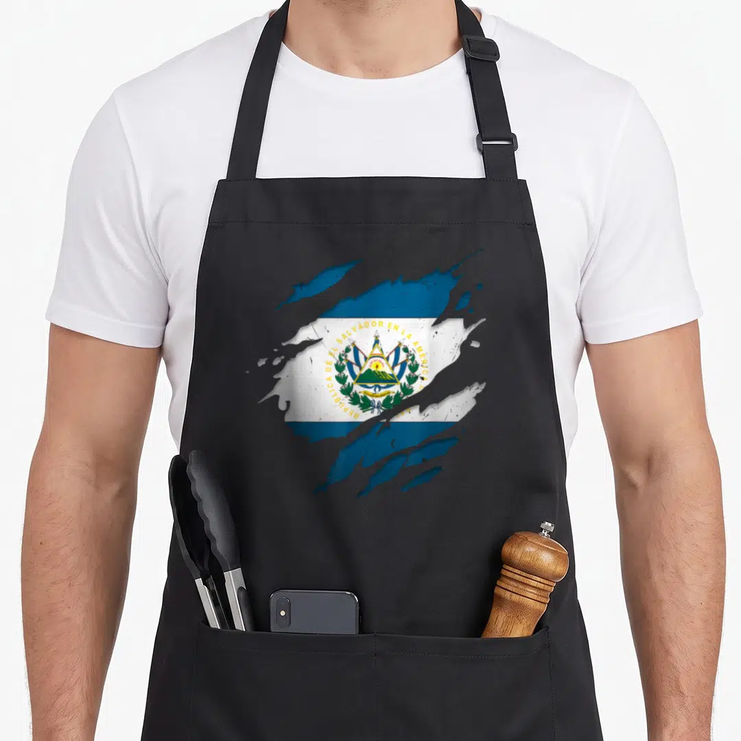 Ripped salvadoran apron - El Salvador flag appearing through torn surface with Republica text in blue white green — shown on a black cotton canvas apron against a white background