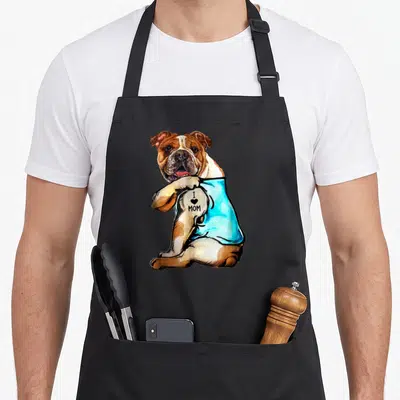 Tattoo english aprons - Cartoon bulldog in blue shirt revealing I Love Mom tattoo on arm — shown on a black cotton canvas apron against a white background