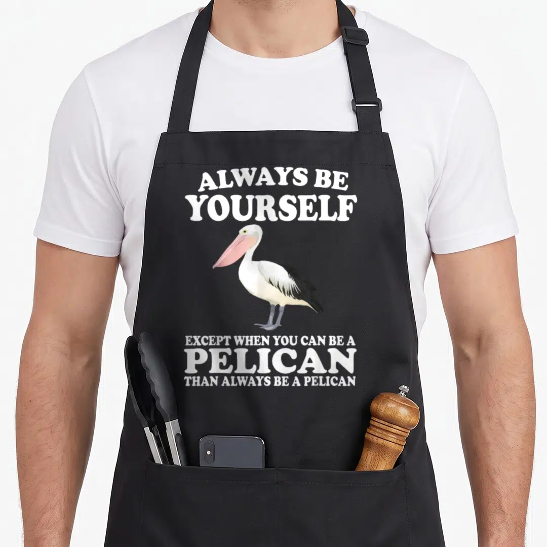 Except always yourself apron - Cartoon pelican in white black pink with text Always Be Yourself Except When You Can Be — shown on a black cotton canvas apron against a white background