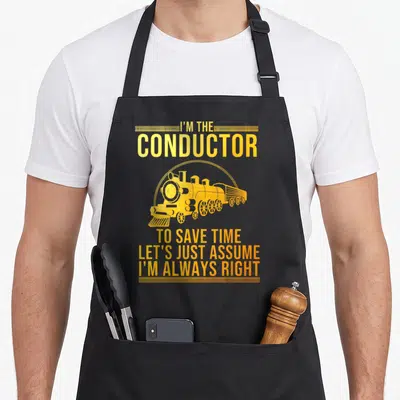 Conductor railway railroad train apron - Yellow steam locomotive flanked by sarcastic conductor text and decorative — shown on a black cotton canvas apron against a white background