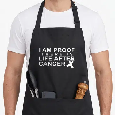 Proof cancer survivor apron - White stacked text reading I AM PROOF THERE IS LIFE AFTER CANCER with a small awareness — shown on a black cotton canvas apron against a white background