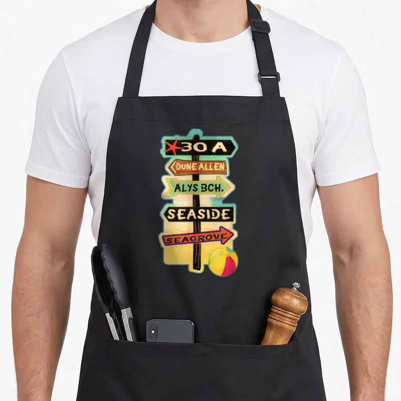 30a florida apron - Cartoon signpost with five directional signs listing coastal towns and a beach ball — shown on a black cotton canvas apron against a white background