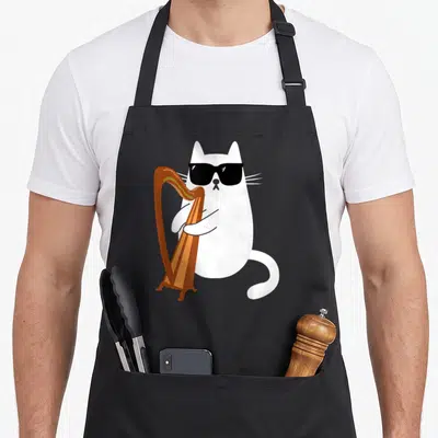 Harp cat wearing apron - White cartoon cat with black sunglasses holding a brown harp — shown on a black cotton canvas apron against a white background