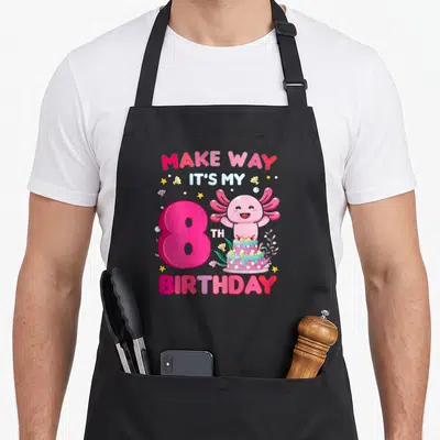 Way 8th birthday apron - Pink axolotl with number 8, cake, and birthday text surrounded by stars and bubbles — shown on a black cotton canvas apron against a white background