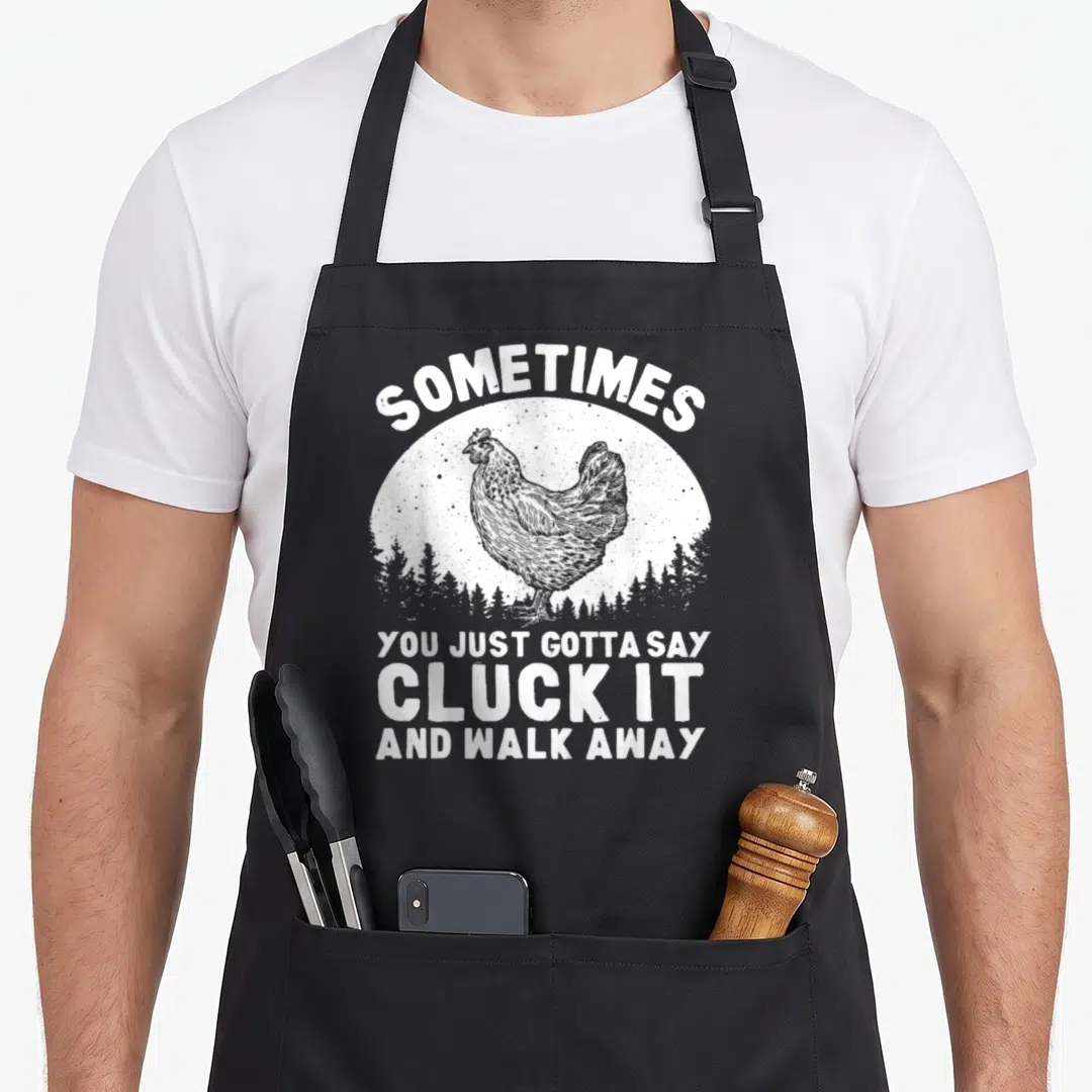 Farmer hen apron - Distressed chicken in white sun with forest silhouette and cluck it quote — shown on a black cotton canvas apron against a white background
