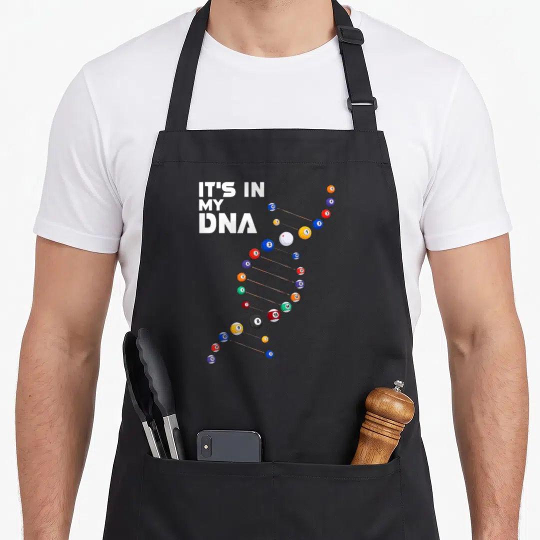 Dna billiards apron - Billiard balls arranged in a DNA helix shape next to stacked white text reading It's In My DNA — shown on a black cotton canvas apron against a white background