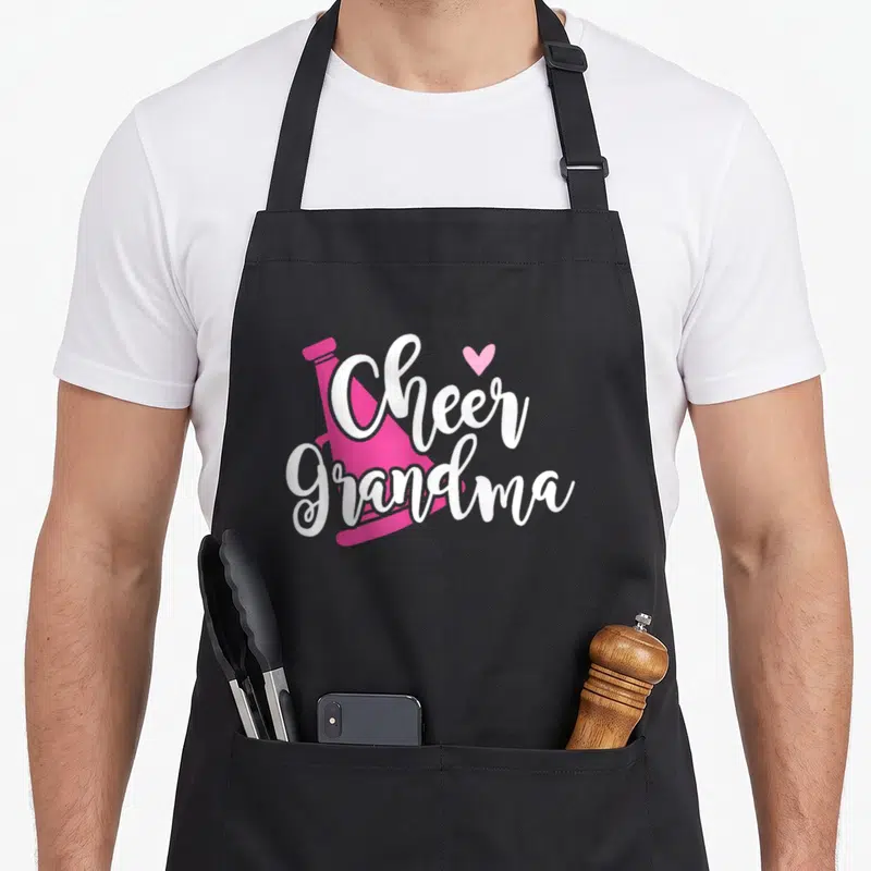 Cheer grandma apron - Pink megaphone with white Cheer Grandma script and small heart — shown on a black cotton canvas apron against a white background