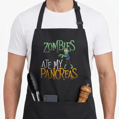Zomby diabetes awareness apron - Cartoon zombie with green skin and text Zombies Ate My Pancreas in green orange — shown on a black cotton canvas apron against a white background