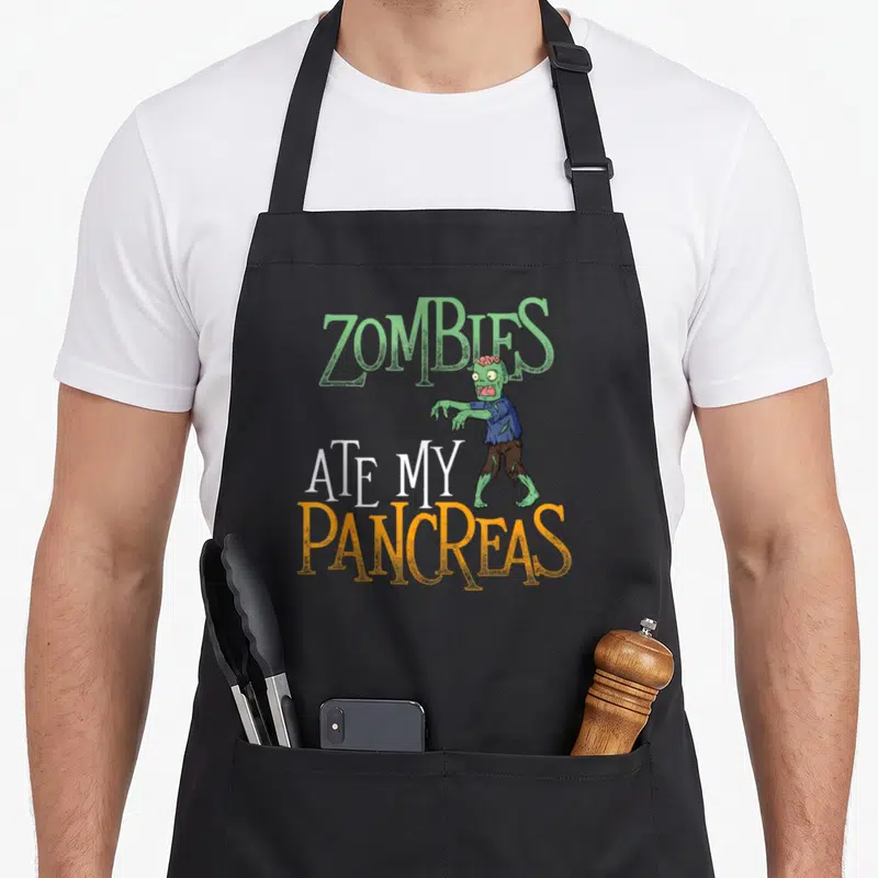 Zomby diabetes awareness apron - Cartoon zombie with green skin and text Zombies Ate My Pancreas in green orange — shown on a black cotton canvas apron against a white background