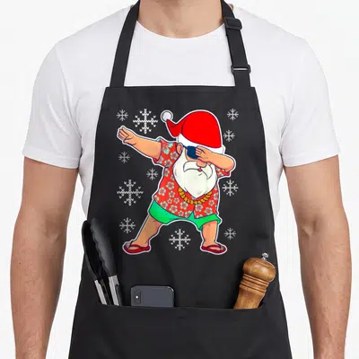 Dabbing tropical print aprons - Cartoon Santa dabbing in red floral shirt and green shorts with white snowflakes — shown on a black cotton canvas apron against a white background
