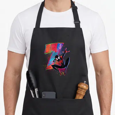 Morale 7th birthday apron - Miles Morales in black suit posing next to colorful glitch art number seven with halftone — shown on a black cotton canvas apron against a white background