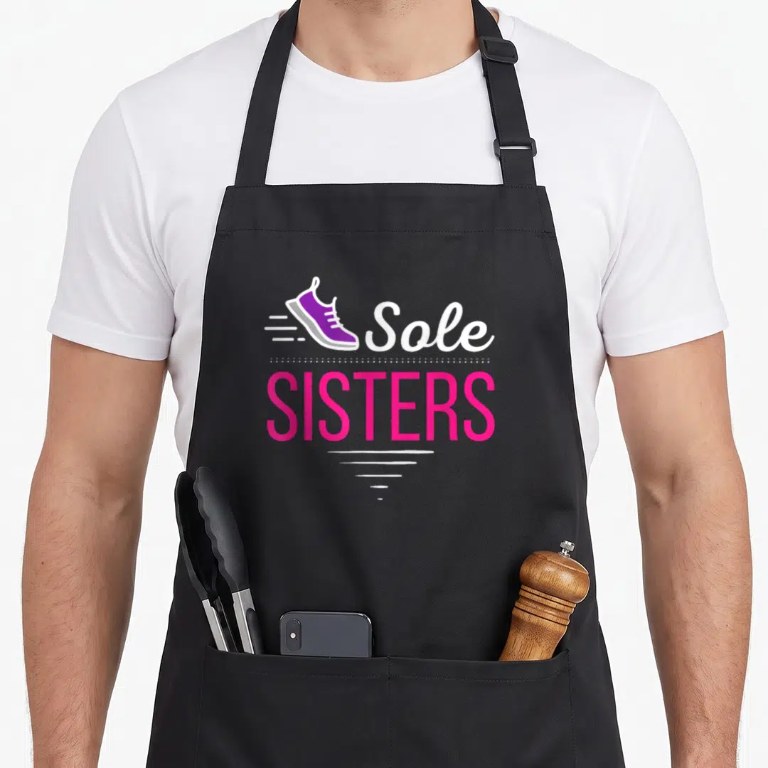 Sister running lover apron - Purple sneaker with Sole SISTERS text and pink lettering — shown on a black cotton canvas apron against a white background