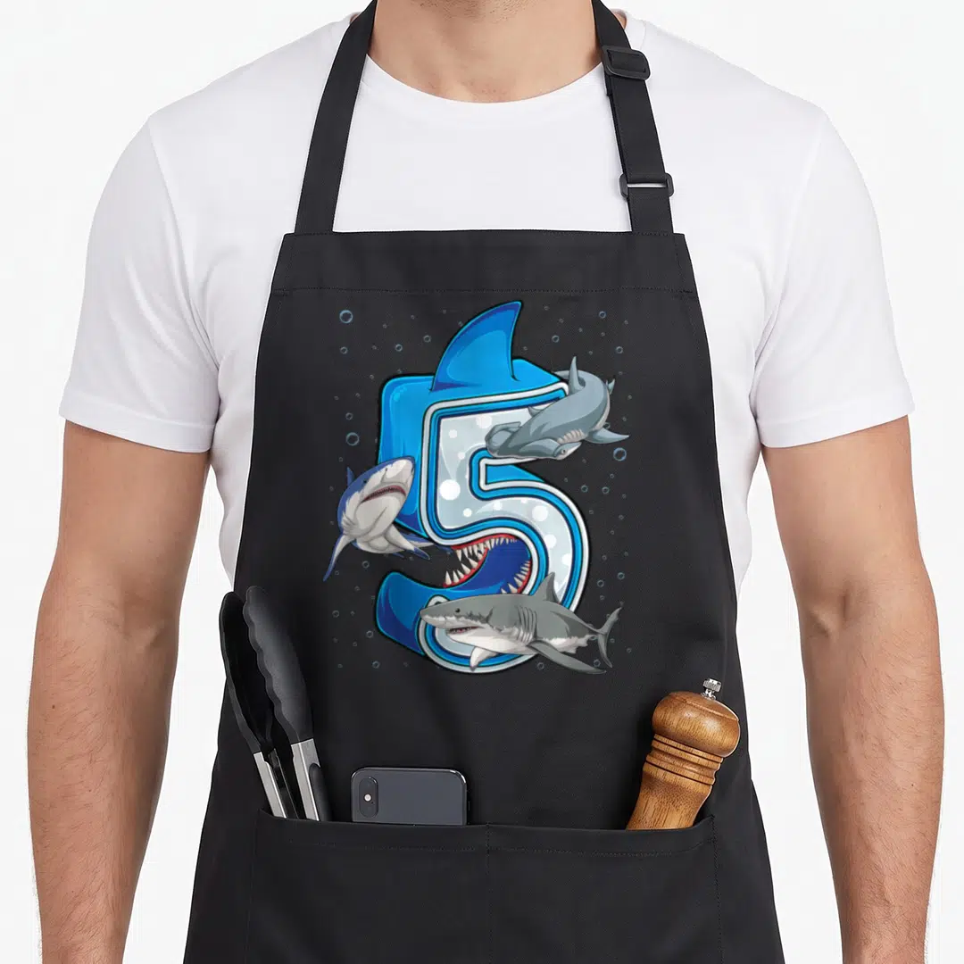 Ocean birthday apron - Large number 5 with three sharks and bubbles in blue, grey, and white cartoon art — shown on a black cotton canvas apron against a white background