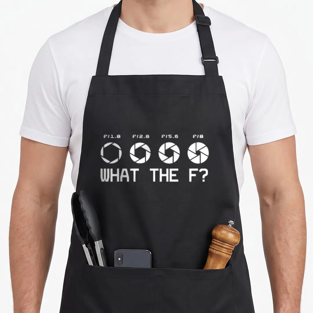 Stop photographer apron - Four white aperture diagrams with f-stop labels and text reading what the f — shown on a black cotton canvas apron against a white background