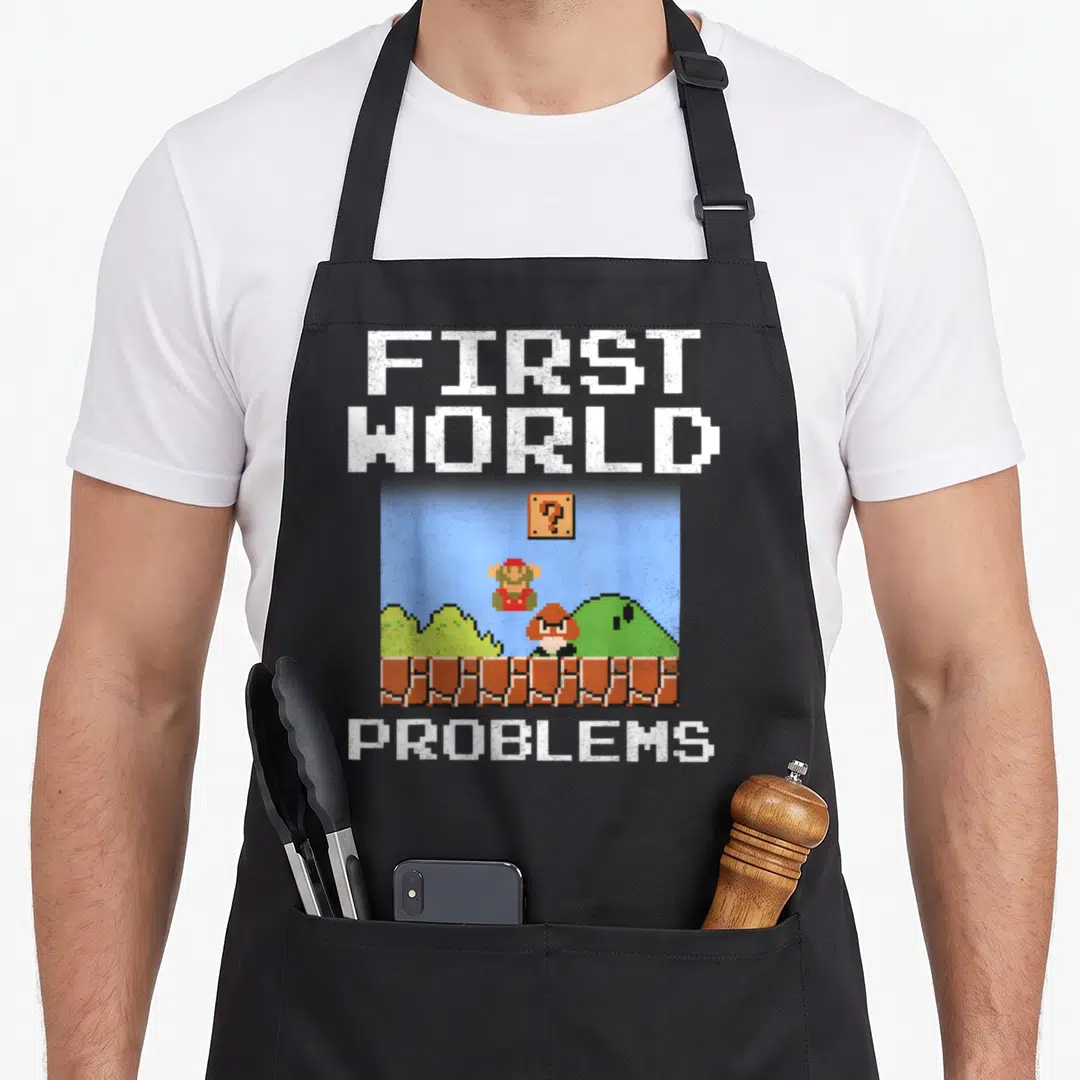 Bit novelty apron - Pixel art Mario and Toad on brick platform under question block with First World Problems text — shown on a black cotton canvas apron against a white background