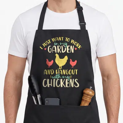Garden hen apron - Stacked text I JUST WANT TO WORK in my GARDEN AND HANGOUT with my CHICKENS with three cartoon — shown on a black cotton canvas apron against a white background
