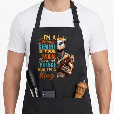 Strong gemini king apron - Stacked text reading I'm a Strong Gemini Black Man next to a crowned man with words — shown on a black cotton canvas apron against a white background