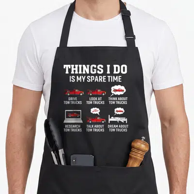 Driver towing truck apron - Red tow trucks in grid with white text reading Things I Do Is My Spare Time — shown on a black cotton canvas apron against a white background