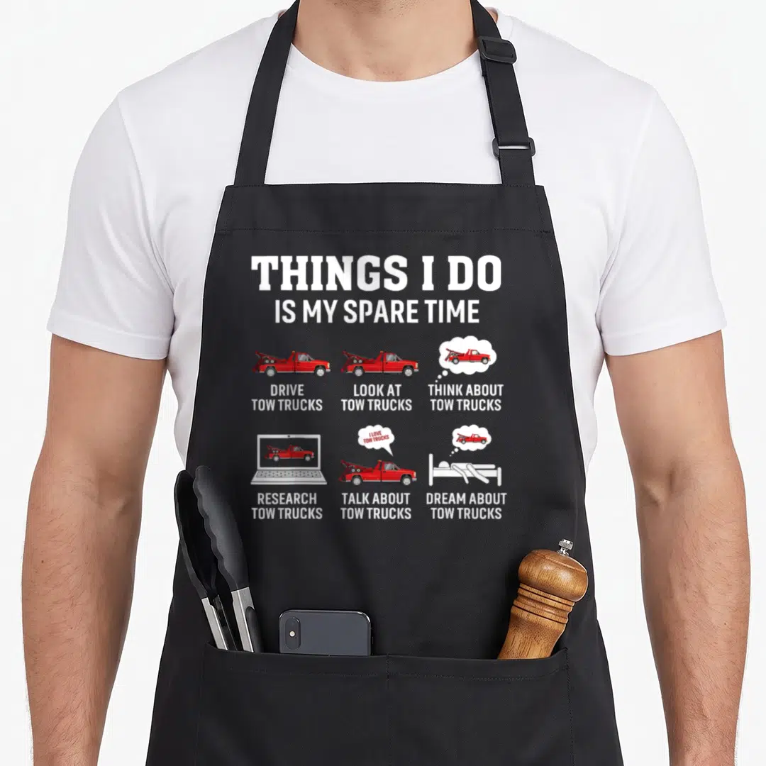 Driver towing truck apron - Red tow trucks in grid with white text reading Things I Do Is My Spare Time — shown on a black cotton canvas apron against a white background