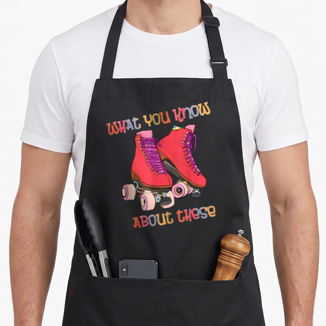 Skate 80s apron - Red quad roller skates with pink laces and arched multicolored text — shown on a black cotton canvas apron against a white background