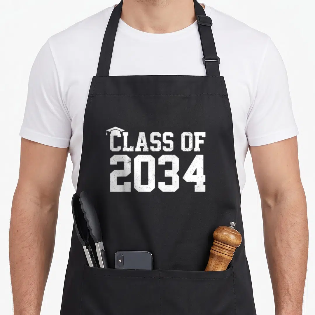 Graduation class apron - Distressed white text reading Class of 2034 with a small graduation cap icon to the top left — shown on a black cotton canvas apron against a white background