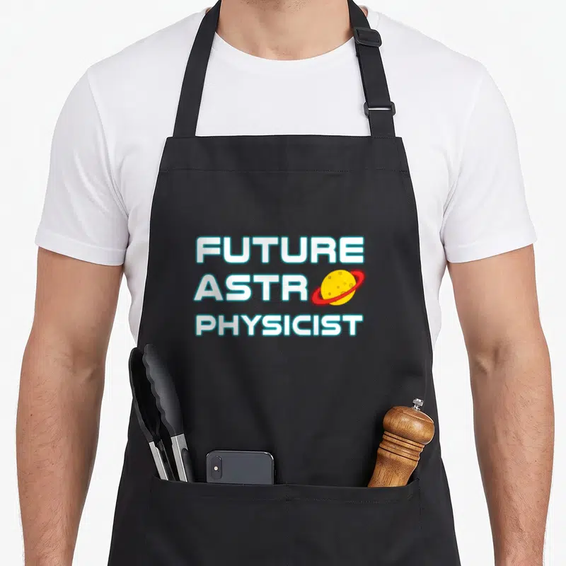 Astrophysic science apron - Stacked FUTURE ASTR PHYSICIST text with yellow planet and red ring replacing a letter — shown on a black cotton canvas apron against a white background