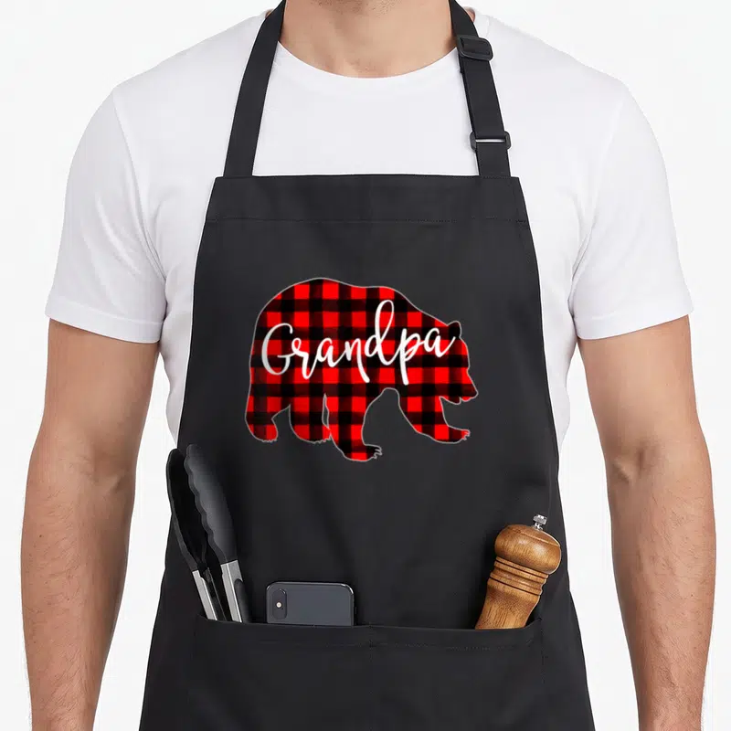 Grandpa buffalo plaid christmas apron - Red and black plaid bear silhouette with white Grandpa script text — shown on a black cotton canvas apron against a white background